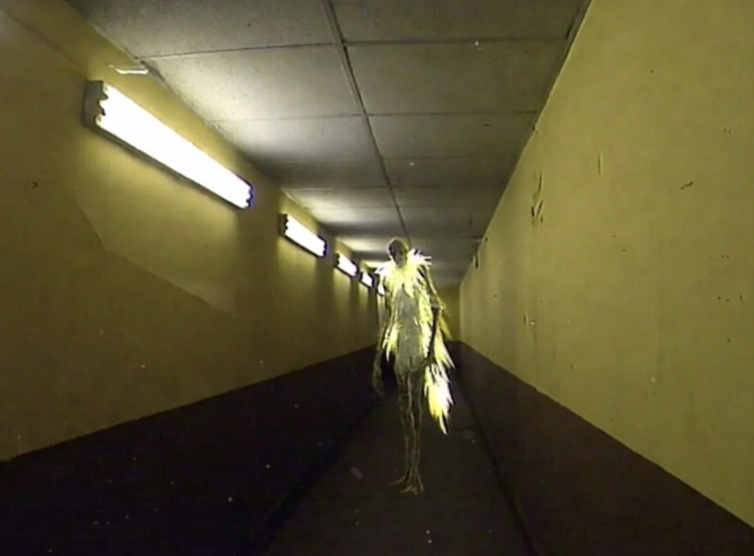 a tall pale figure covered in yellow feathers standing in a yellow corridor