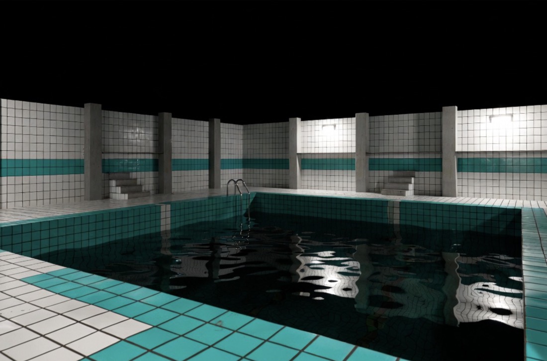 a dark tiled pool room, teal water reflecting fluorescent light, no one swimming